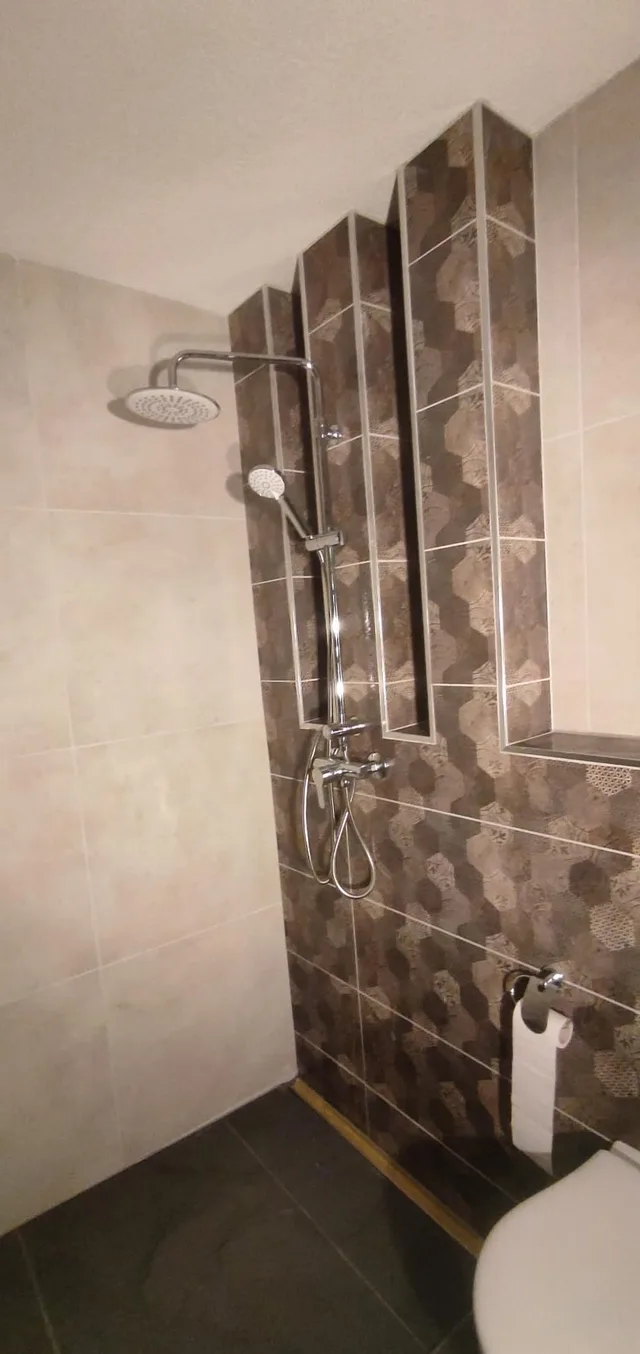 Dusch- und WC-Bereich mit heller Seitenwand, dunkel gemusterter Akzentfläche, gestaffelten Vorsprüngen und Duscharmatur
