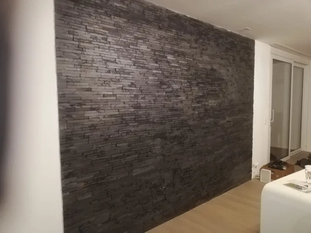Grossflächige Innenwand mit dunklen Riemchen in unterschiedlichen Längen neben hellen Wandflächen und Holzboden