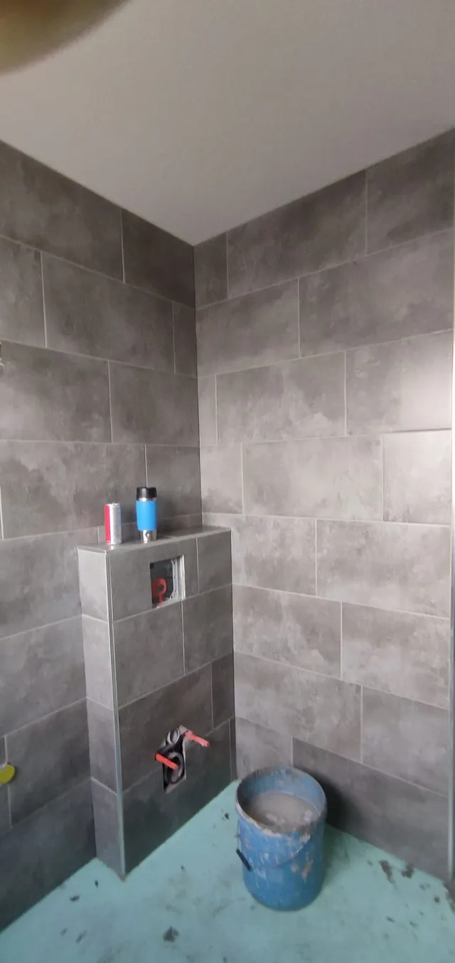 Seitliche Ansicht der grauen WC-Vorwand und der raumhoch bekleideten Wandflächen bei noch offenem Bodenaufbau.