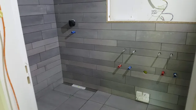 Breite Wandansicht im grauen Bad mit schmalem Rechteckverband, zahlreichen offenen Installationspunkten und belegtem Boden.