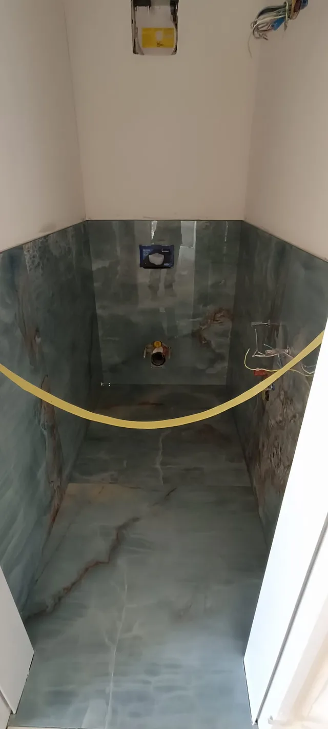 Kleiner Sanitärraum im Ausbau mit grün-blauen Platten an Boden und halbhohen Wänden sowie offenen Leitungs- und Elektroanschlüssen.