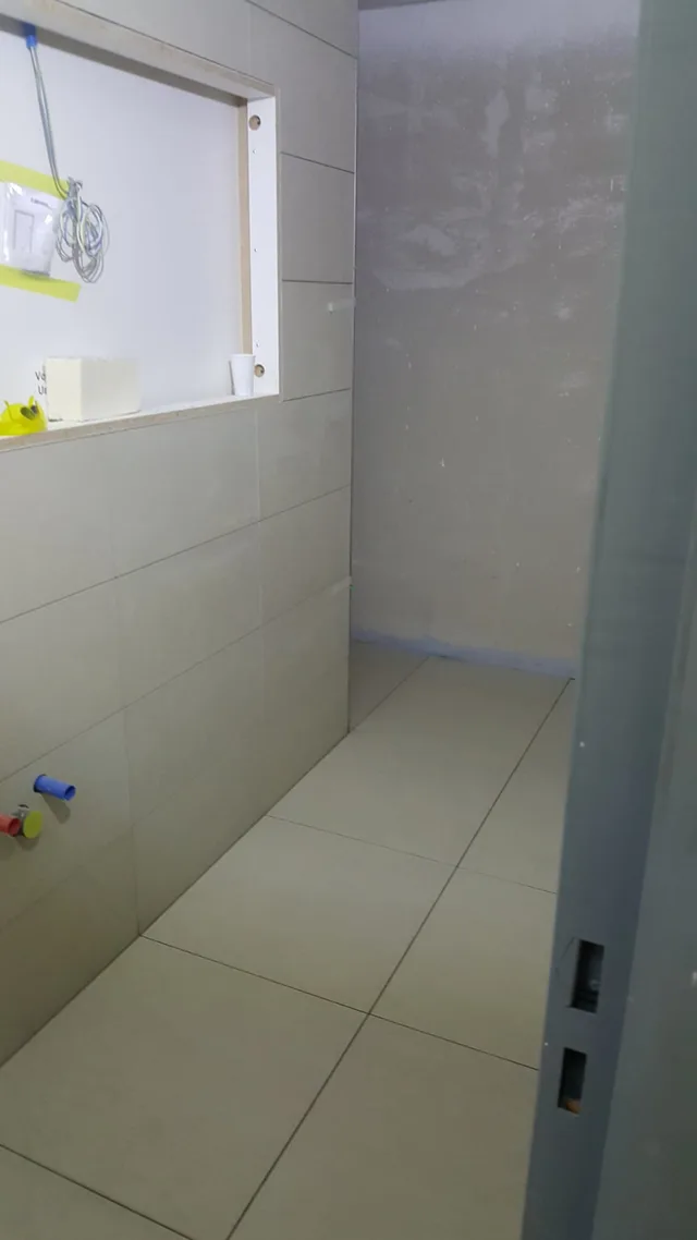 Schmaler Sanitär- oder Nebenraum im Ausbau mit hellem Boden, teilbekleideter Wand, Fenster und grosser offener Einbauöffnung.