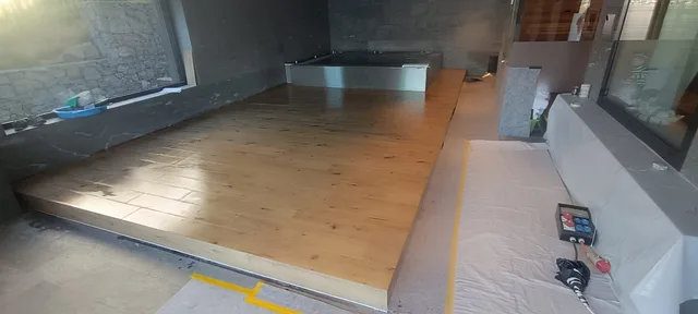 Breite Raumansicht der erhöhten Holzoptik-Plattform mit Poolbecken im Hintergrund und geschütztem Arbeitsbereich an der Seite.
