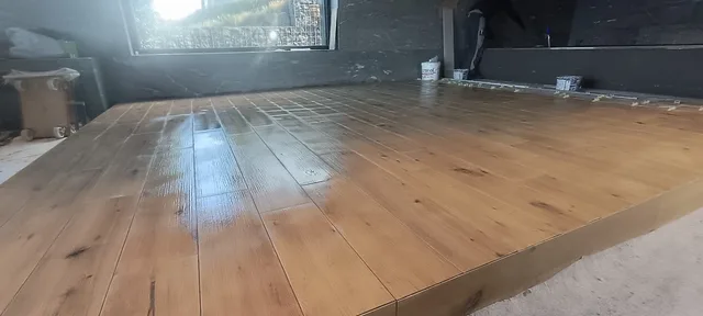 Niedrige Nahansicht der Holzoptik-Platten auf der erhöhten Plattform mit sichtbarer Vorderkante und dunkler Wand im Hintergrund.