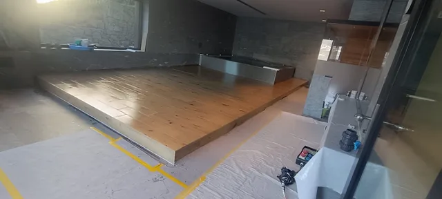 Weite Ansicht vom Zugang auf die erhöhte Holzoptik-Plattform, das Poolbecken und die geschützten Randbereiche des Raumes.