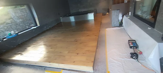 Erhöhter Blick entlang der Holzoptik-Plattform zum Poolbecken, mit belegter Seitenkante und abgedecktem Arbeitsweg rechts.