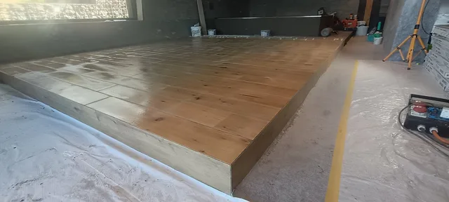 Erhöhte Plattform im Poolraum mit länglichen Holzoptikplatten, belegter Stirnseite und geschützten Baustellenwegen rundherum.